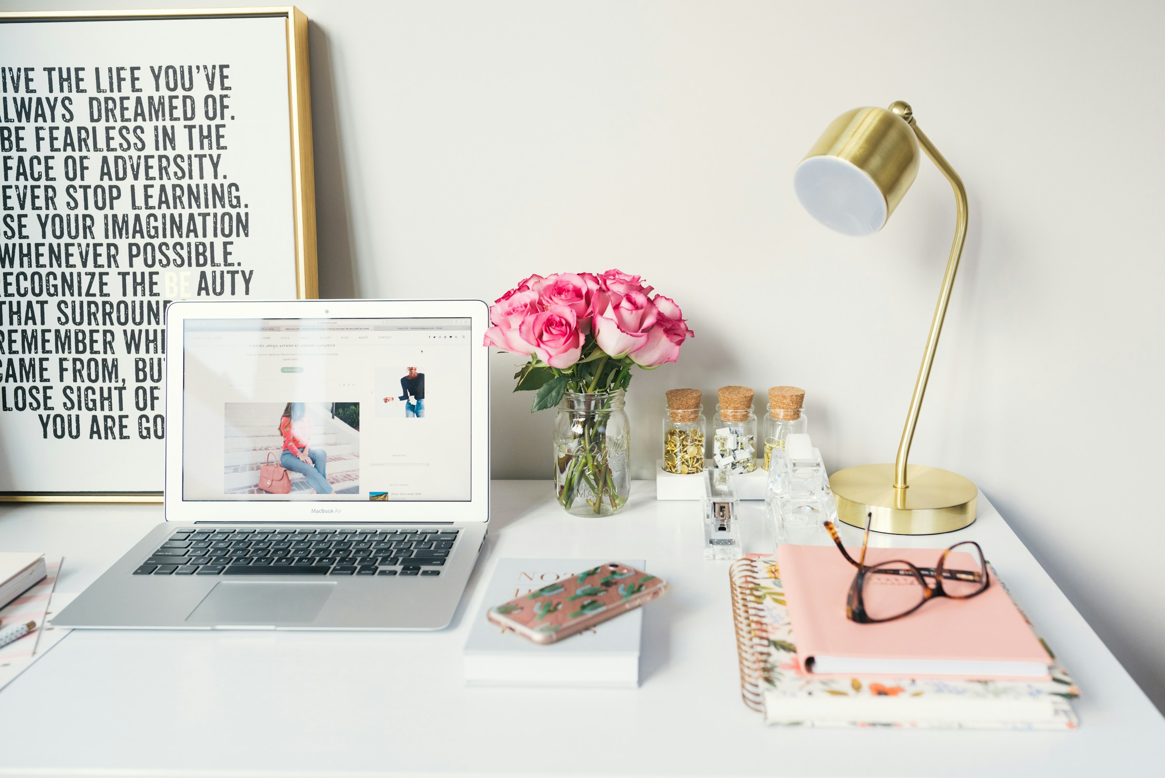Image of a sleek table with a poster, open laptop, bunch of roses, stationary and a lamp.
Photo by Arnel Hasanovic on Unsplash