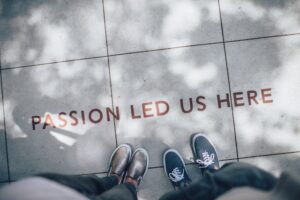 The words 'Passion Led Us Here' are stamped on the floor. The camera is facing down at it and you can see two feet facing the words.
Photo by Ian Schneider on Unsplash